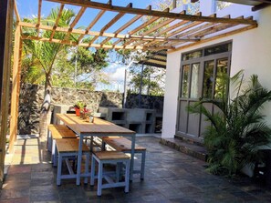 Une terrasse extérieure dotée d’une pergola en bois, de murs en pierre et d’un espace détente avec des bancs et des tables.