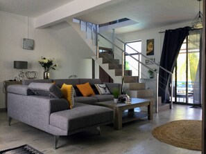 Ein modernes Wohnzimmer mit einem grauen Ecksofa, einem Couchtisch und einer Treppe, die zu einer oberen Ebene führt.