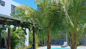 Zona de piscina con palmeras, un área de estar cubierta y un edificio con ventanas.