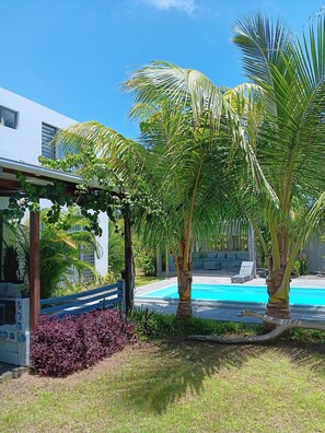 A pool area with palm trees, a covered seating area, and a building with windows. - Serene 3-Bedroom Villa with Private Pool in Roches Noires (Roches Noires)