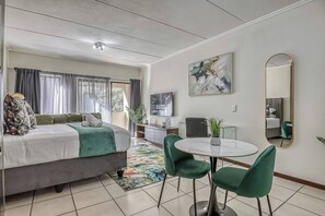 Une chambre d’hôtel moderne équipée d’un lit, d’une table à manger avec des chaises, d’un téléviseur et d’un grand miroir.