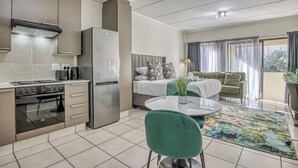 Una cucina moderna con piano cottura, forno e frigorifero, un'area pranzo con tavolo e sedie, e un balcone con divano e tende.