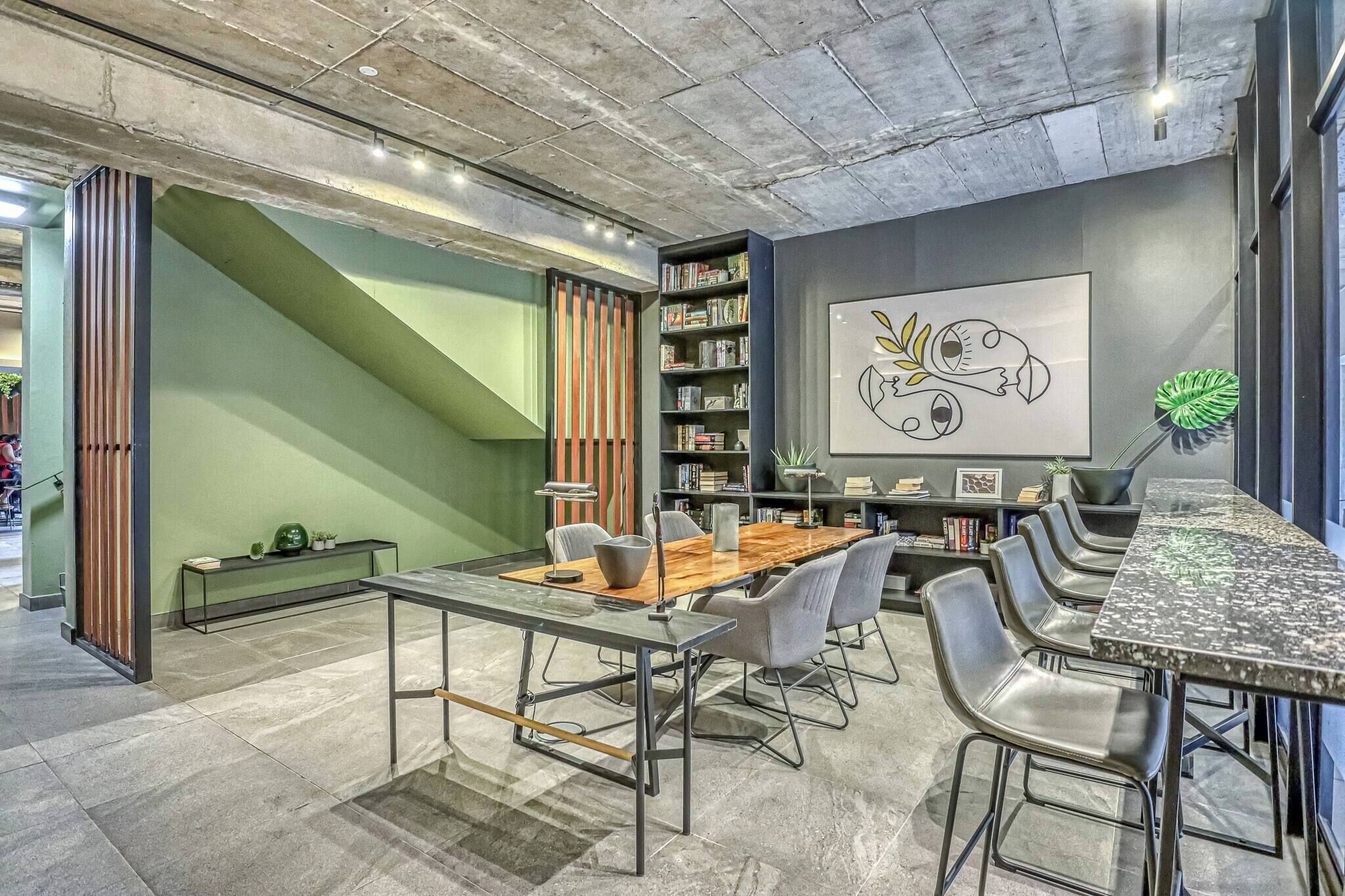 A modern conference room with a wooden table, metal chairs, a bookshelf, and a large abstract painting on the wall.