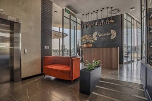 Um hall moderno com balcão de recepção, um sofá vermelho, uma planta em vaso e vista através de grandes janelas.