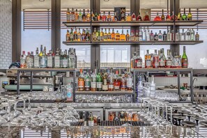 Uma área de bar com prateleiras cheias de garrafas de bebidas e muitos copos.