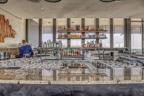 Eine Bar mit Barkeeper, Regalen voller Spirituosenflaschen und zahlreichen Gläsern.