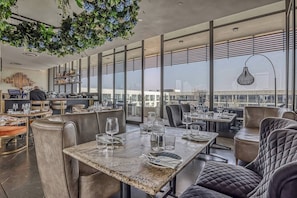Un restaurante moderno con techos altos, amplios ventanales y vistas a la ciudad.