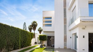 A modern building with a paved walkway, a neatly trimmed hedge, and a palm tree in the background. - Luxurious Villa Rental in Tunis with Private Indoor Pool (Tunis)
