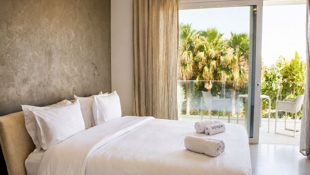 A modern hotel room with a large bed, a balcony with a view of palm trees, and a sliding glass door. - Luxurious Villa Rental in Tunis with Private Indoor Pool (Tunis)
