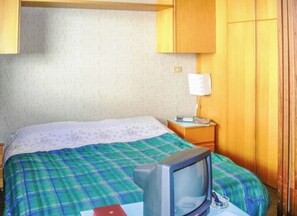 Una habitación con una cama, televisión, mesita de noche y lámpara.
