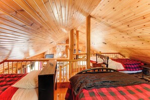 L’intérieur d’une cabane en bois, avec une chambre à coucher située en mezzanine, un escalier et une vue sur l’extérieur.