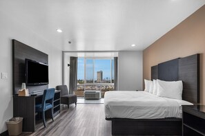 A hotel room with a bed, desk, chair, TV, and a large window with a view of a building. - 1 King Bed|Nsmk|Micfridge|View (Oceanside)