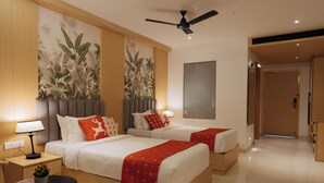 A hotel room with two beds, a ceiling fan, a nightstand with a lamp, and a wall-mounted TV.