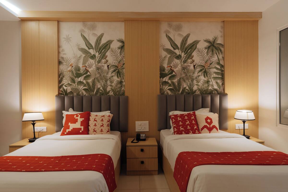 Habitación de hotel con dos camas, una mesita de noche entre ellas, un mural en la pared y una lámpara en el techo.