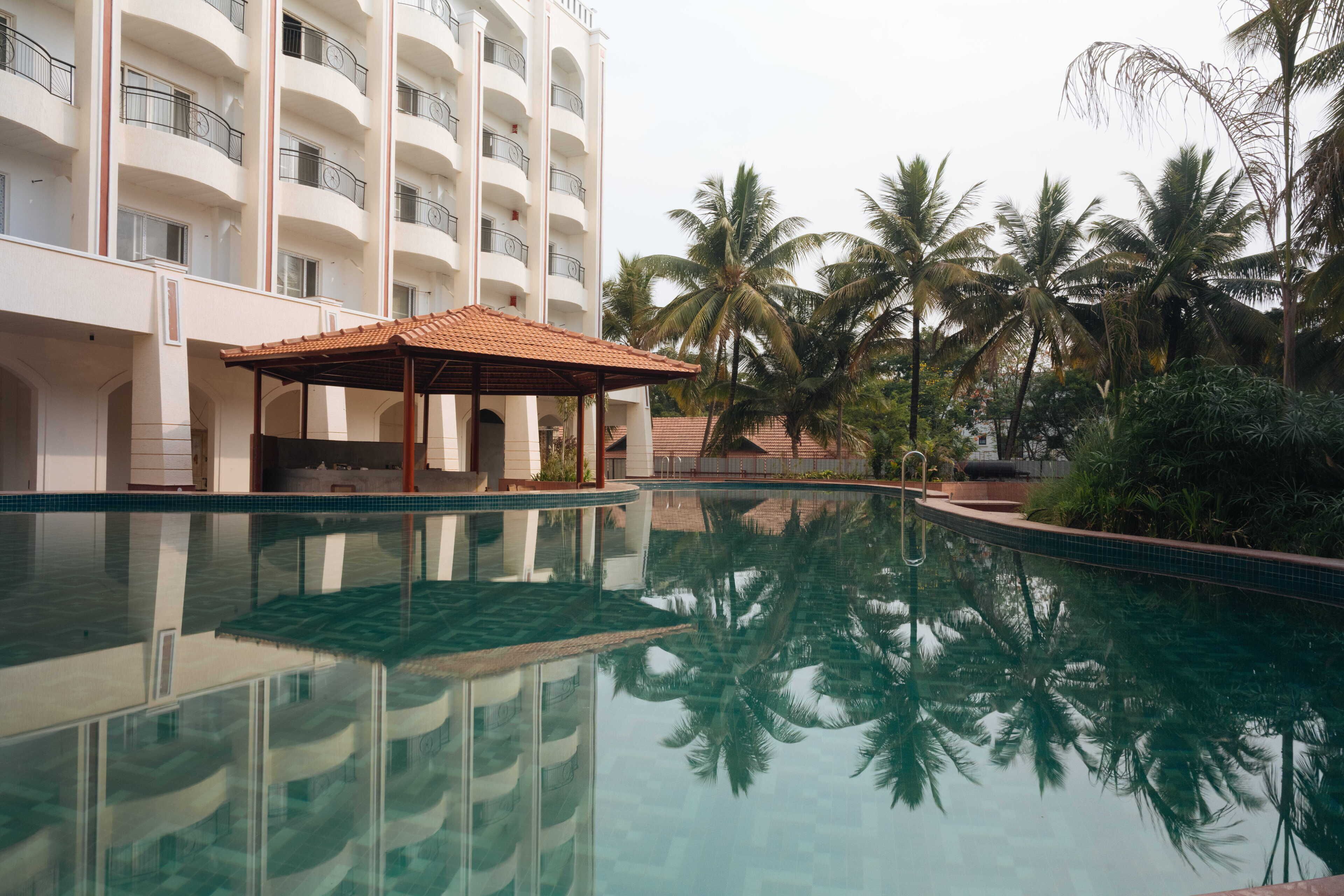 A swimming pool with a reflection of palm trees and a building with balconies.