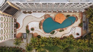 An aerial view of a hotel with a large heart-shaped pool, palm trees, and a tiled walkway.