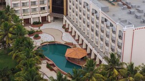 A hotel with a swimming pool, palm trees, and a rooftop with air conditioning units.