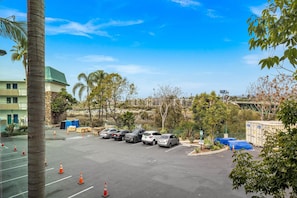 A parking lot with several cars, a palm tree, and a building with a green roof.