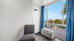 A room with a gray chair, a window with blue curtains, and a view of a parking lot. - 1 Queen Bed|Nsmk,Micfridge,View (Oceanside)