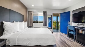A modern hotel room with a large bed, a desk with a chair, a television, and a balcony with a view. - 1 Queen Bed|Nsmk,Micfridge,View (Oceanside)