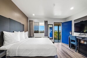 Una camera d'albergo moderna con un letto grande, una scrivania con una sedia, una televisione a schermo piatto e un balcone con vista.
