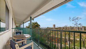 En balkon med bord og stole, udsigt over et boligområde, og et grønt gelænder.