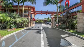 Entrada de hotel con un arco rojo, palmeras y un letrero que indica 6 habitaciones y disponibilidad de Wi-Fi.