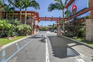 A hotel entrance with a red archway, palm trees, and a sign indicating 6 rooms and Wi-Fi availability.