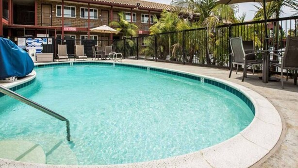 Ein Pool mit Liegestühlen und Sonnenschirmen, umgeben von einem Zaun und Palmen.