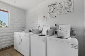 Un lavadero con dos lavadoras de carga frontal, un secador y una lavadora montada en la pared. Se observan letreros que dicen 'Easy Washing' y 'Servicio'.