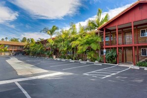 A hotel with a parking lot, palm trees, and a red building facade. - 2 Queen Beds|Suite,Micfridge (Carlsbad)