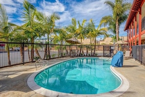 Ein Swimmingpool mit umgebender Einfriedung, Palmen und einem Gebäude mit roter Fassade.