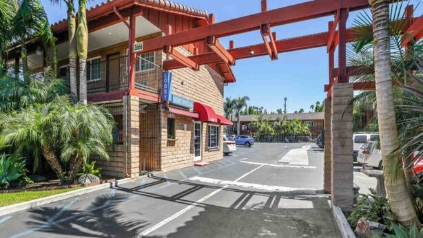 A hotel entrance with a red archway, a lobby sign, and a parking area with cars.