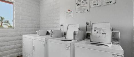 A laundry room with two front-loading washers, a dryer, and a wall-mounted washing machine. There are signs for 'Easy Washing' and 'Service' on the wall.