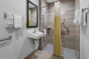 Ein modernes Badezimmer mit Waschbecken, Spiegel, Dusche und Haltegriffen.