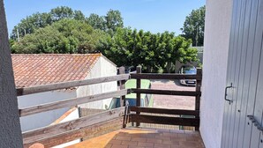 En balkon med gelænder af træ, udsigt til en grøn bil og en bygning med et tag af tegl.