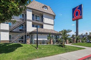 Un motel à deux étages, avec un toit recouvert de tuiles, un balcon au deuxième étage et une enseigne indiquant qu’il s’agit d’un motel proposant également des studios.