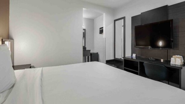 A hotel room with a bed, a desk with a computer, a flat-screen TV, and a mirror.