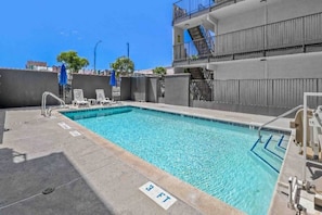 A rooftop swimming pool with clear blue water, a diving board, and a staircase leading to an upper level.