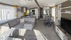 Een modern camperinterieur met een bank, eettafel, televisie en keuken.