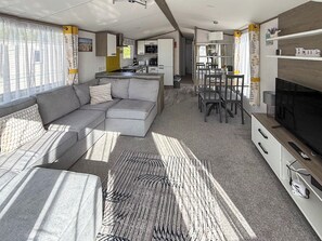 A modern RV interior with a sofa, dining table, TV, and kitchen area. - Horse Shoe Lakes - UKC9581 (Mablethorpe)