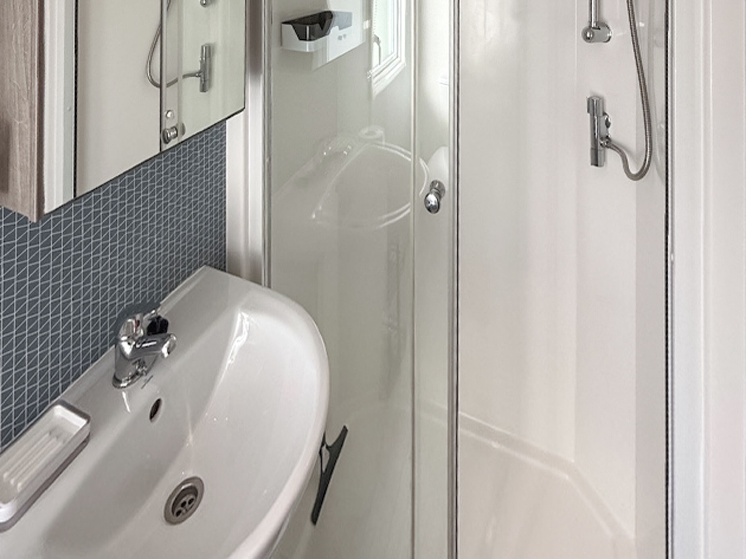 Ein Badezimmer mit einem weißen Waschbecken, einem Spiegel und einer Duschkabine aus Glas.
