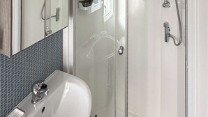 Een badkamer met een wit wastafelmeubel, een spiegel en een douchecabine met glazen wanden.