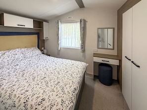 Ein Schlafzimmer mit einem Bett, einem Nachttisch, einem Spiegel, einem Fenster mit Vorhängen und einem Kleiderschrank.