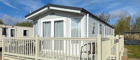 A mobile home with a fenced deck, a covered porch, and a small attached garage.