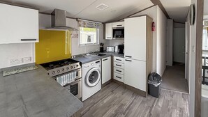 Een kleine keuken met een fornuis, wasmachine, magnetron en kastjes.