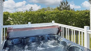Un bain à remous doté d’une structure métallique, d’un panneau de commande et d’une rambarde en bois.