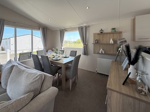 Ein möbliertes Zimmer mit Esstisch, Stühlen, einer Couch, einem Heizkörper und einem Fenster mit Vorhängen.