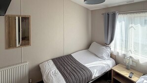 Un lit simple avec une couverture rayée grise et blanche, une table de chevet avec une lampe et une fenêtre avec des rideaux.