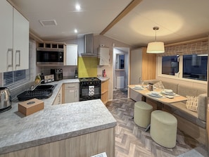A compact kitchen with a central island, a dining area with a bench, and a window with a view. - Golf Village 107 - UKC9578 (Mablethorpe)
